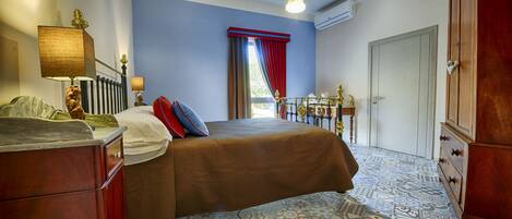 A bedroom with a bed, a dresser, a nightstand, and a window with curtains.
