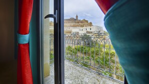 A view from a window with a metal railing, a red curtain, and a glimpse of a historic building in the background.