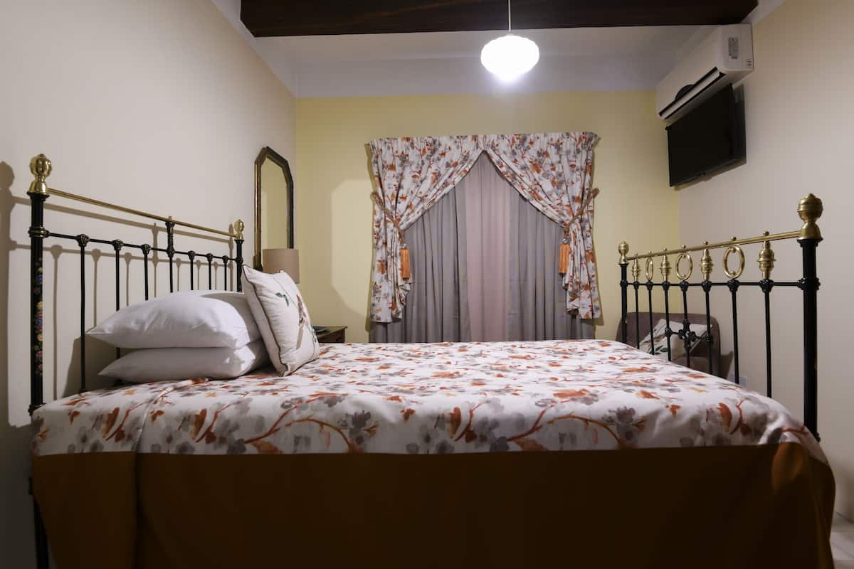 A bed with a floral bedspread, a bedside table, a mirror, and curtains.