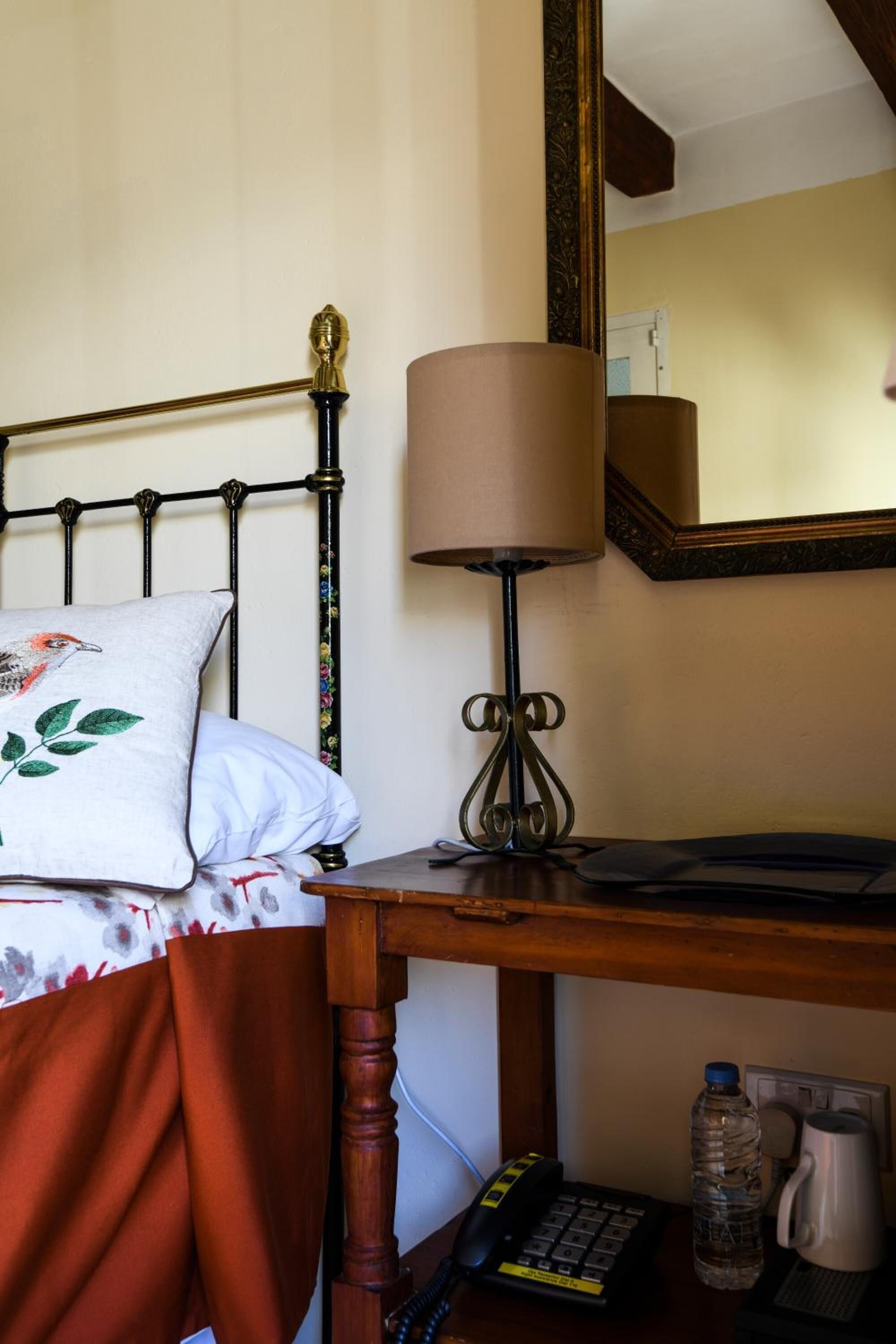 Un letto con un cuscino floreale, una lampada da comodino, un telefono, una bottiglia d'acqua e una macchina per il caffè su un comodino in legno.