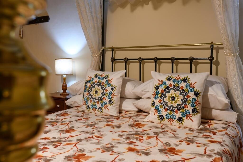 A bed with a floral bedspread and decorative pillows, a bedside lamp, and a metal headboard.