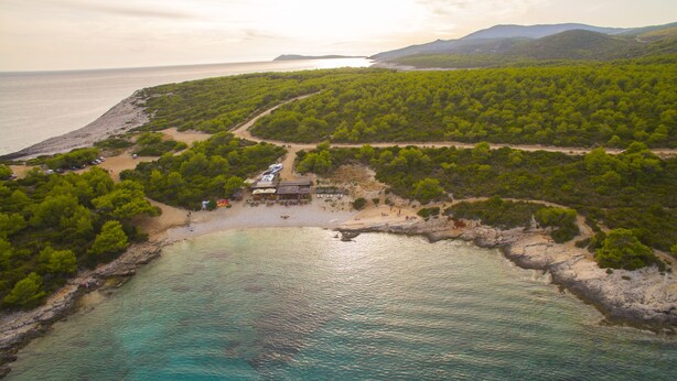 Vista aérea de una zona costera con playa, aguas turquesas cristalinas y vegetación verde exuberante.