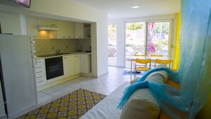 Una cocina compacta con armarios blancos, horno integrado y ventana con vistas a un patio.