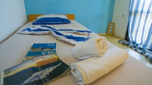 Una cama con un edredón azul y blanco a rayas, una toalla enrollada y un folleto turístico sobre la cama.