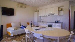 Un espacio habitable compacto con sofá, mesa de comedor, sillas, zona de cocina con armarios y estufa, y un televisor montado en la pared.