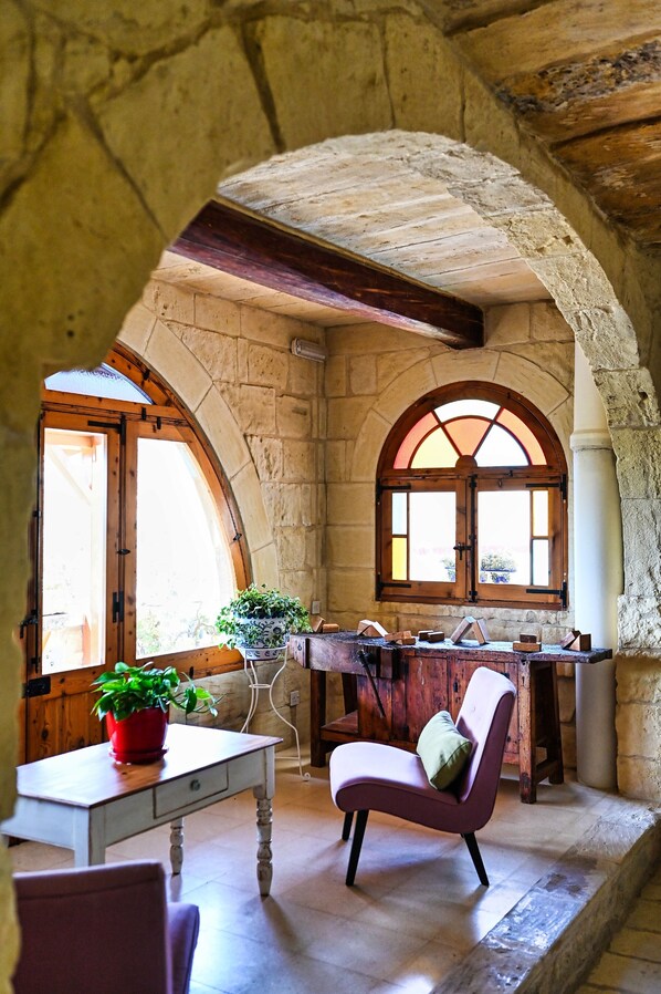 A room with stone walls, a wooden table, a chair, and a window with an arched design. - Maria's B&B (Ghasri)