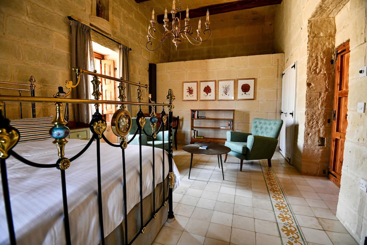A room with a bed, a chandelier, a green armchair, and a bookshelf.