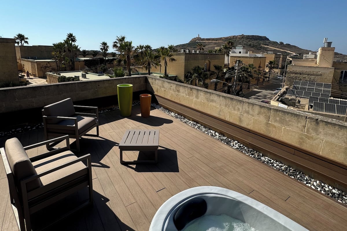 A rooftop terrace with a hot tub, lounge chairs, and a view of the cityscape.