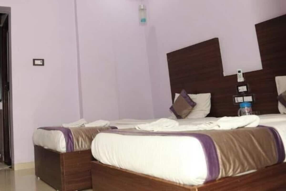 Une chambre d’hôtel avec deux lits, une tête de lit en bois, une petite table de chevet et une salle de bain équipée d’un lavabo et d’un miroir.