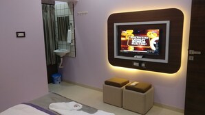 Un baño moderno con una televisión montada que muestra un anuncio promocional, un lavamanos, un espejo y dos taburetes acolchados.