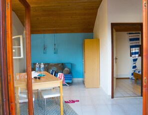 A room with a wooden ceiling, a blue wall, a sofa, a wooden door, and a bed with a striped curtain. - Victorious VIScovery Red (Vis)