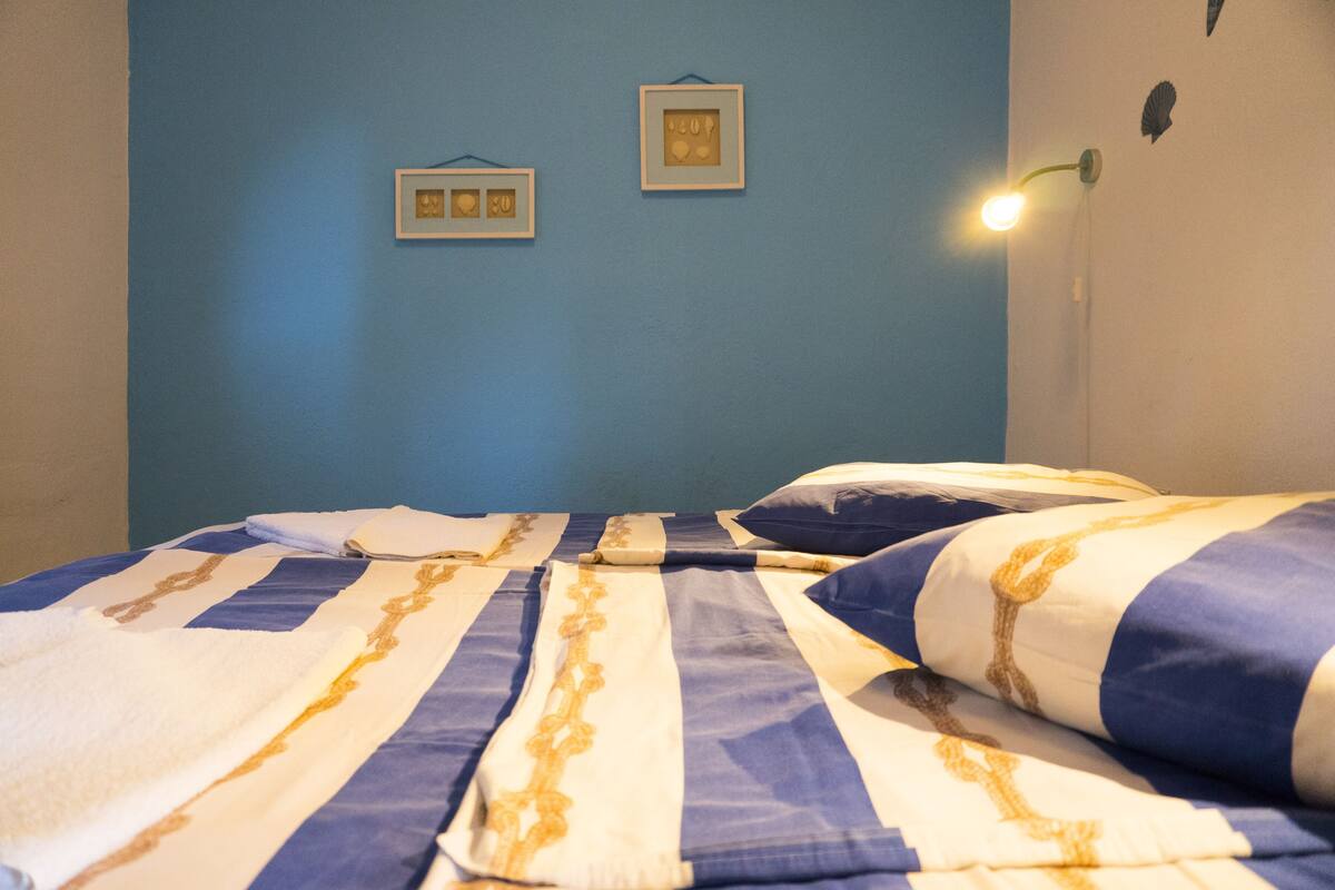 A bed with striped bedding, a wall-mounted light, and two framed pictures on the wall.