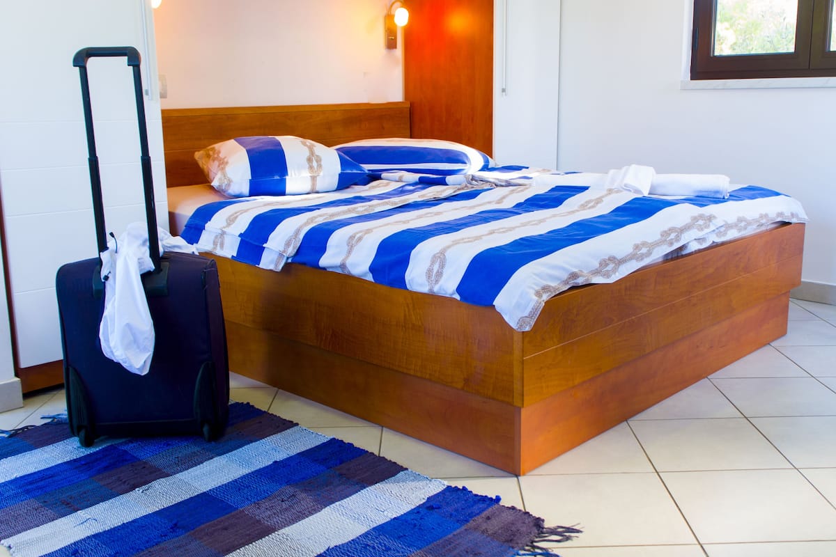 A neatly made bed with a striped bedspread, a wooden headboard, and a suitcase on the floor.