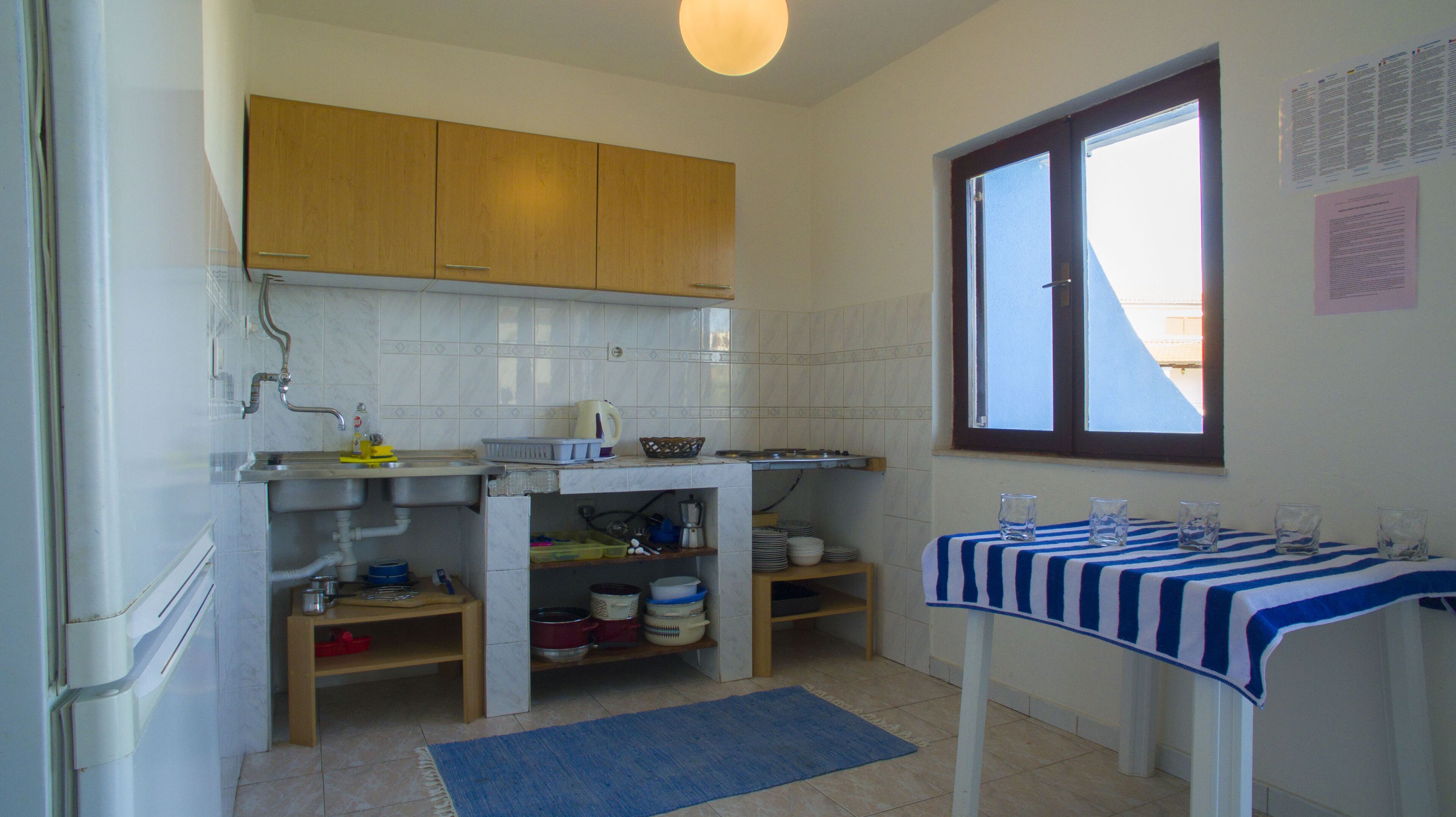 Une cuisine compacte avec des meubles de rangement en bois, un évier, une fenêtre et une table avec des verres.