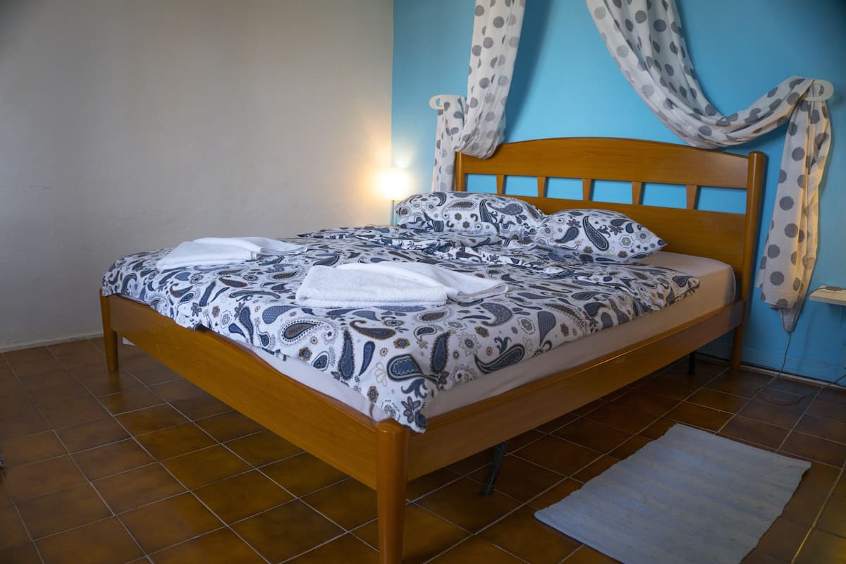 A neatly made bed with a patterned bedspread and pillows, a wooden headboard, and a blue wall with curtains.
