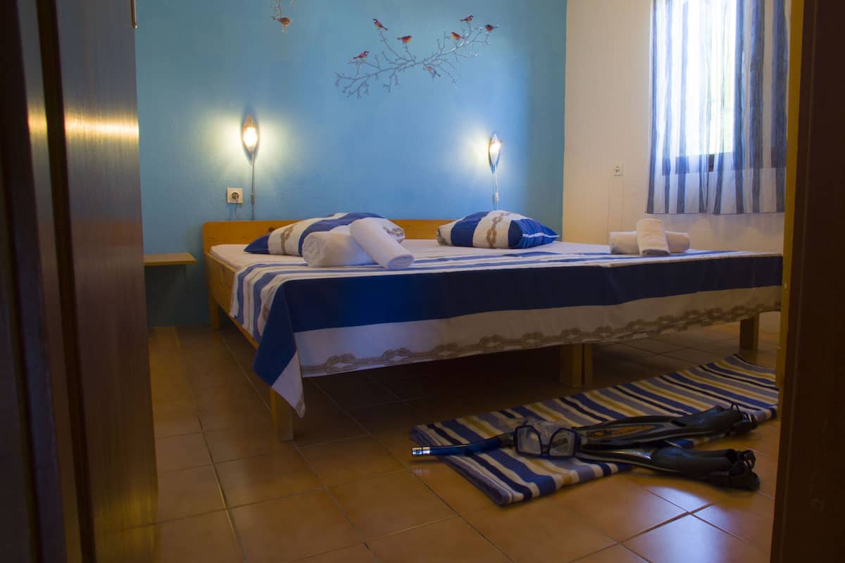 A bedroom with a bed, two wall-mounted lamps, a window with curtains, and a tiled floor.