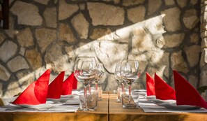 Un tavolo apparecchiato con calici da vino e tovaglioli rossi, sullo sfondo di un muro in pietra.