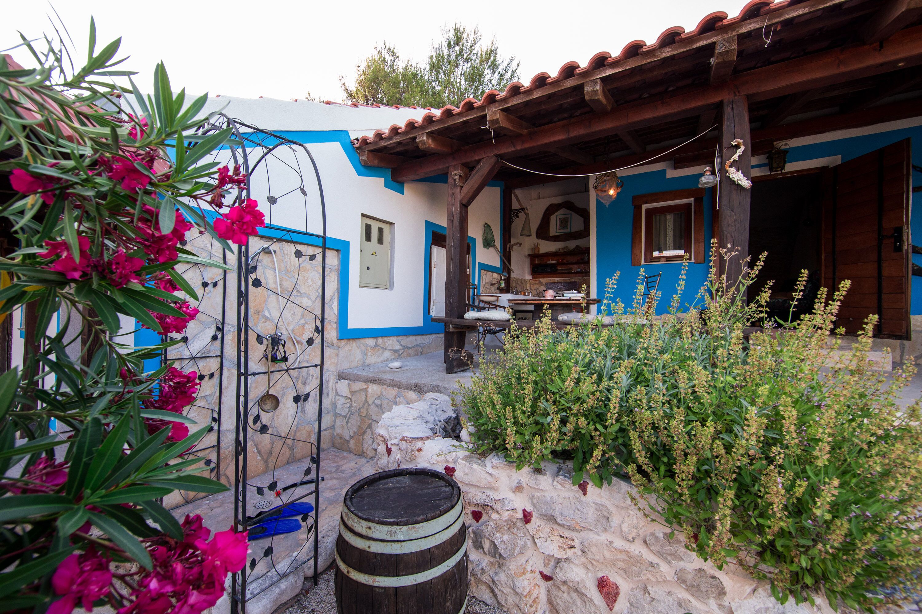A rustic building with a stone wall, a wooden barrel, and a variety of plants.