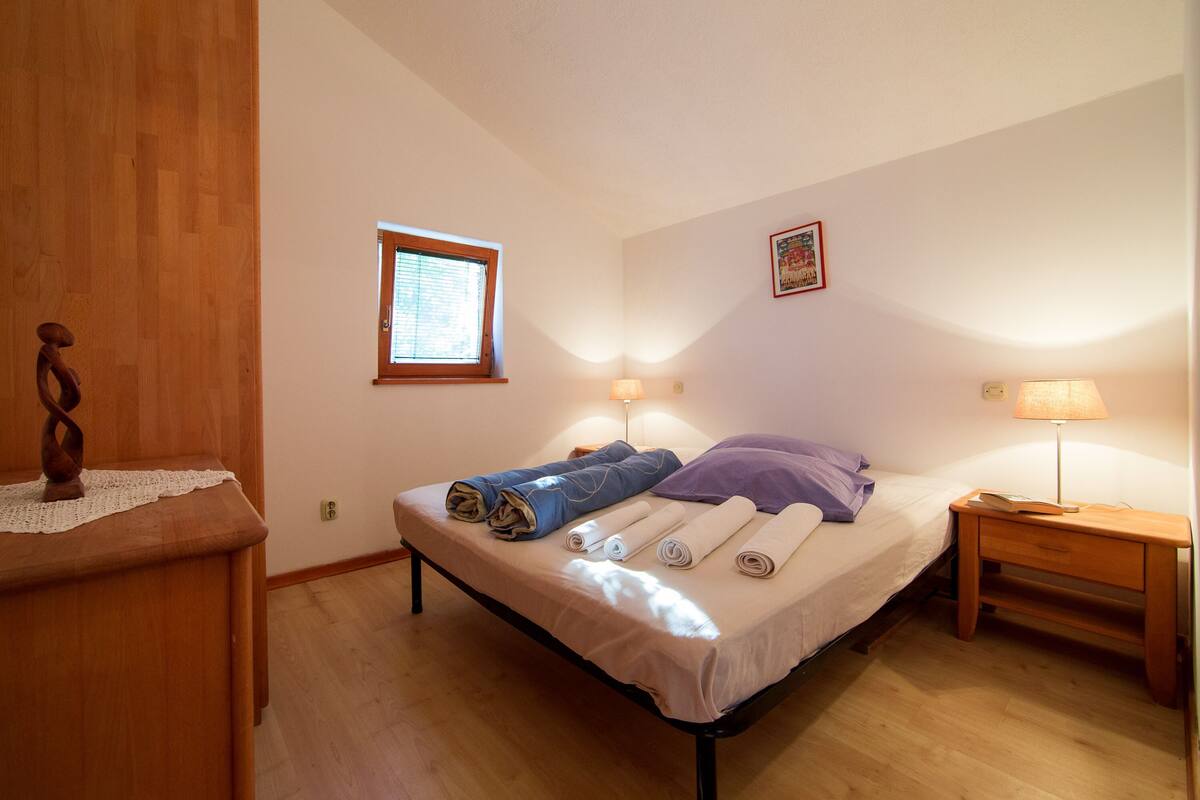 A bedroom with a bed, a nightstand, a window, and a wooden dresser.