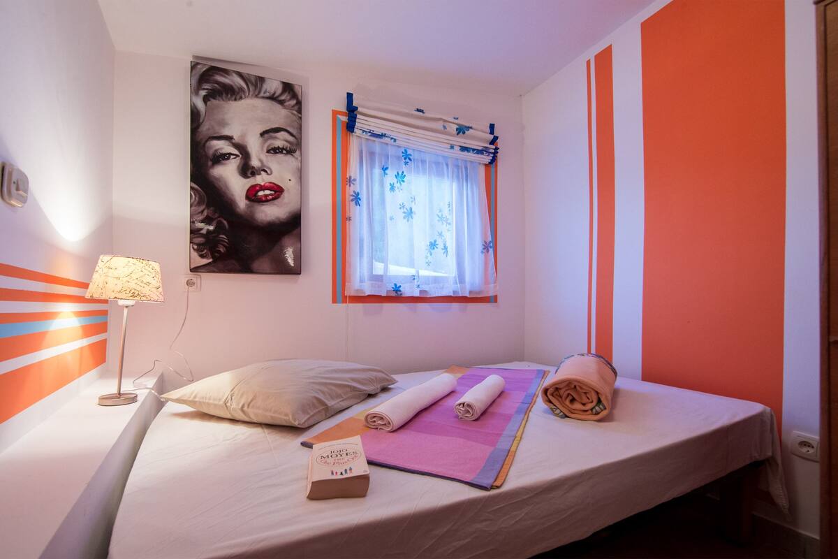 A neatly made bed with a pillow, a rolled towel, and a book on the side.