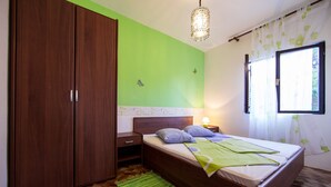 Un dormitorio con cama, mesita de noche, armario, pared verde y ventana con cortinas.