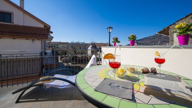 Eine Dachterrasse mit Tisch für zwei Personen, ausgestattet mit einem Getränk, Sonnenbrille und einem Obstkorb.