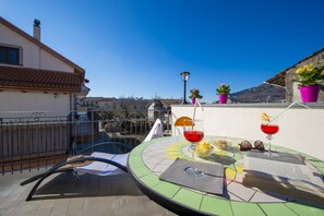 Terraço no telhado com mesa posta para dois, incluindo bebida, óculos de sol e cesta de frutas.