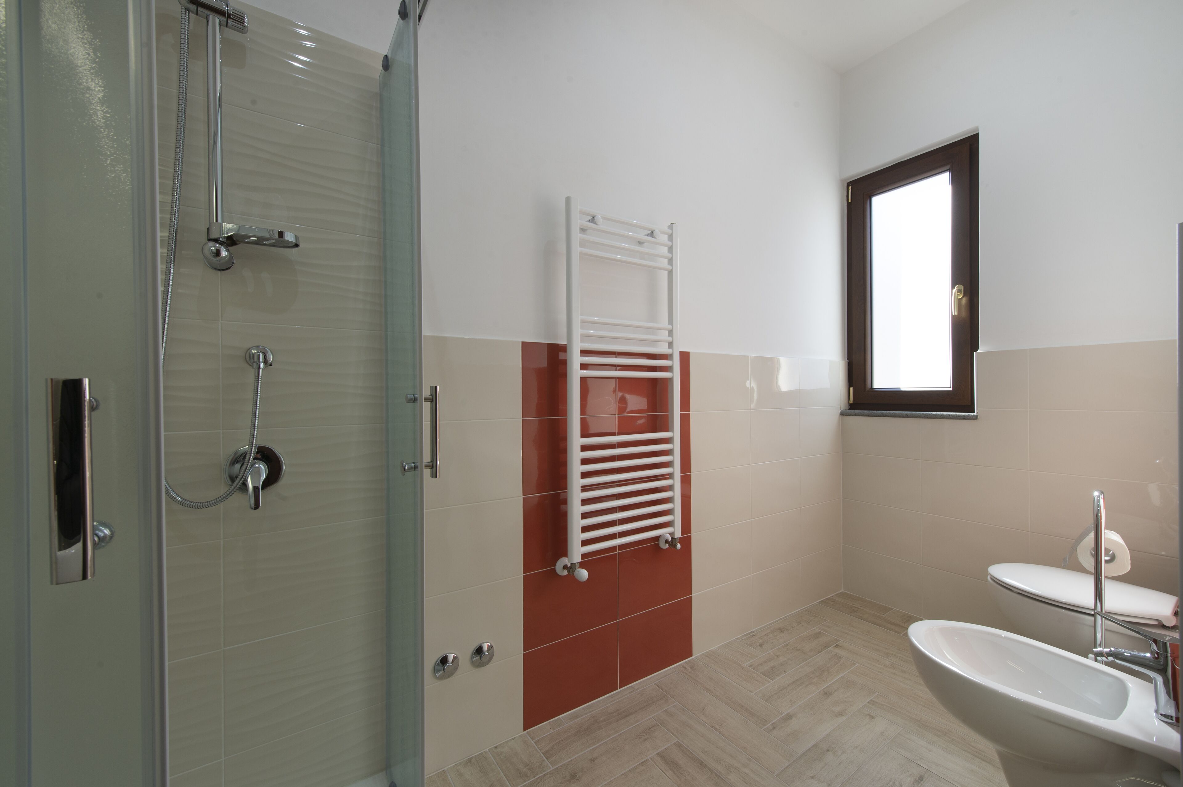 A bathroom with a glass shower enclosure, a white sink, and a red-tiled wall.