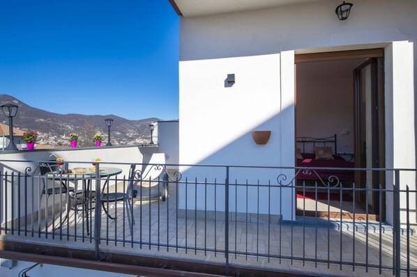 Un balcon avec une table et des chaises, un petit jardin et une vue sur les montagnes.