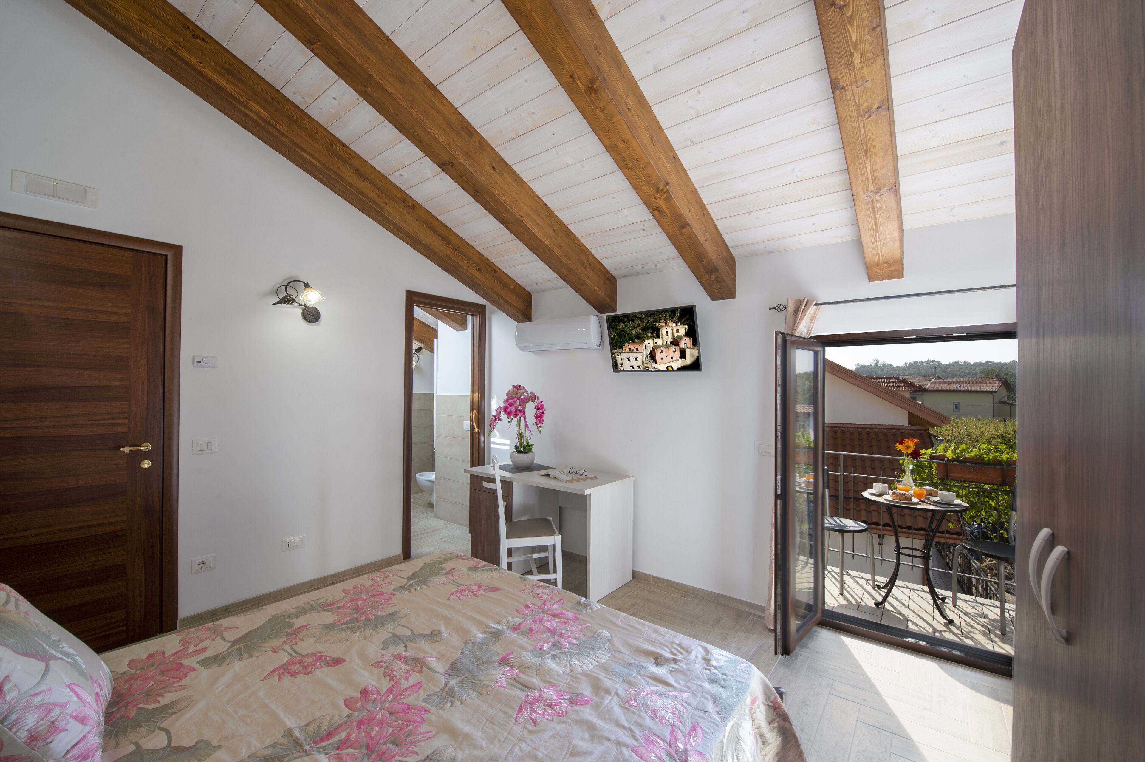 Ein Schlafzimmer mit Bett, Schreibtisch und einem Balkon mit Tisch und Stühlen.