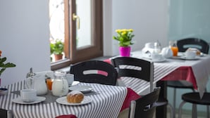 Ein Frühstückstisch mit gestreiftem Tischläufer, einer Karaffe, Tassen, einem Teller mit Gebäck und einer Vase mit gelben Blumen.