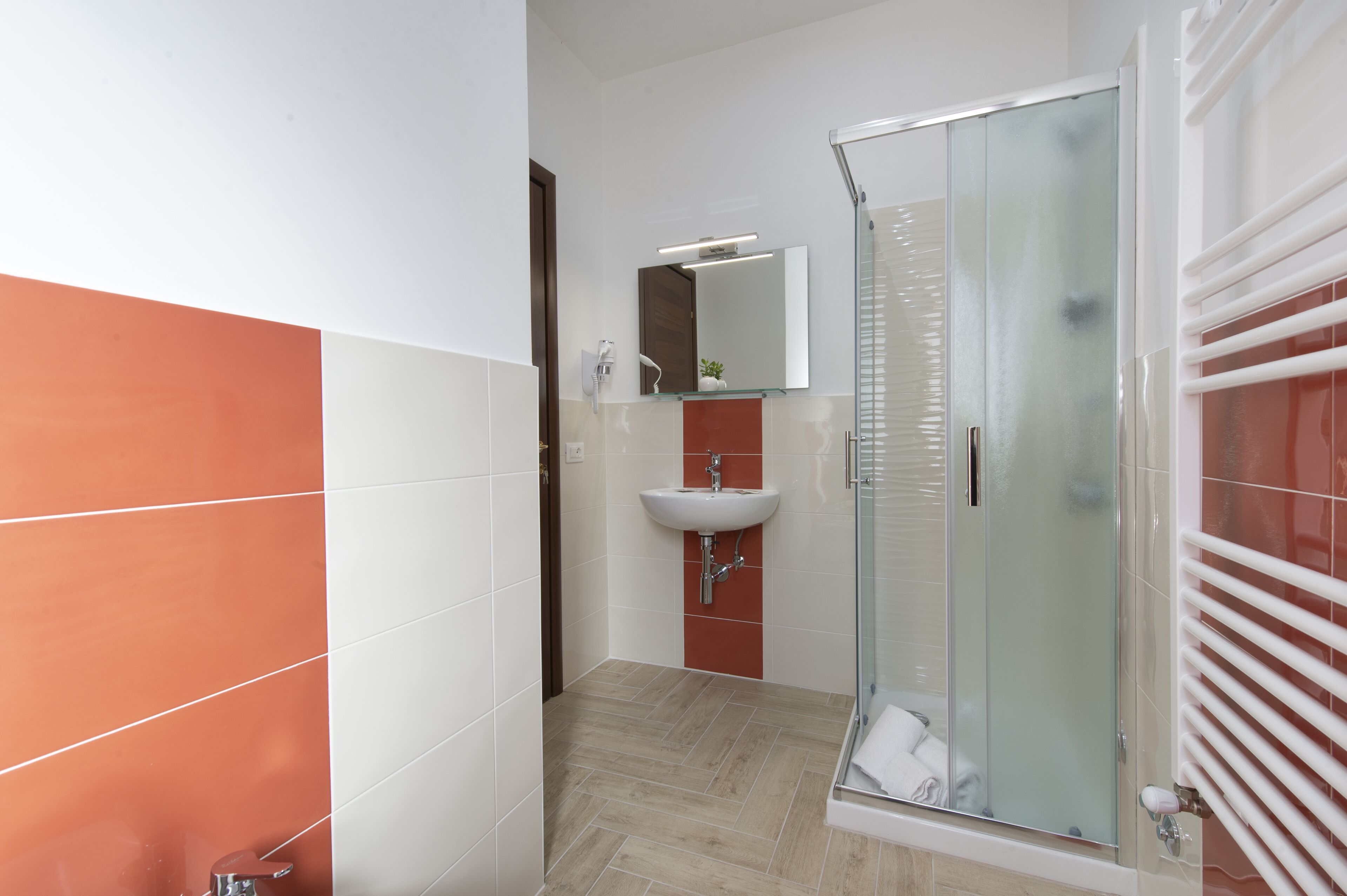 Un baño moderno con cabina de ducha de vidrio, un lavamanos con espejo y suelo de baldosas.