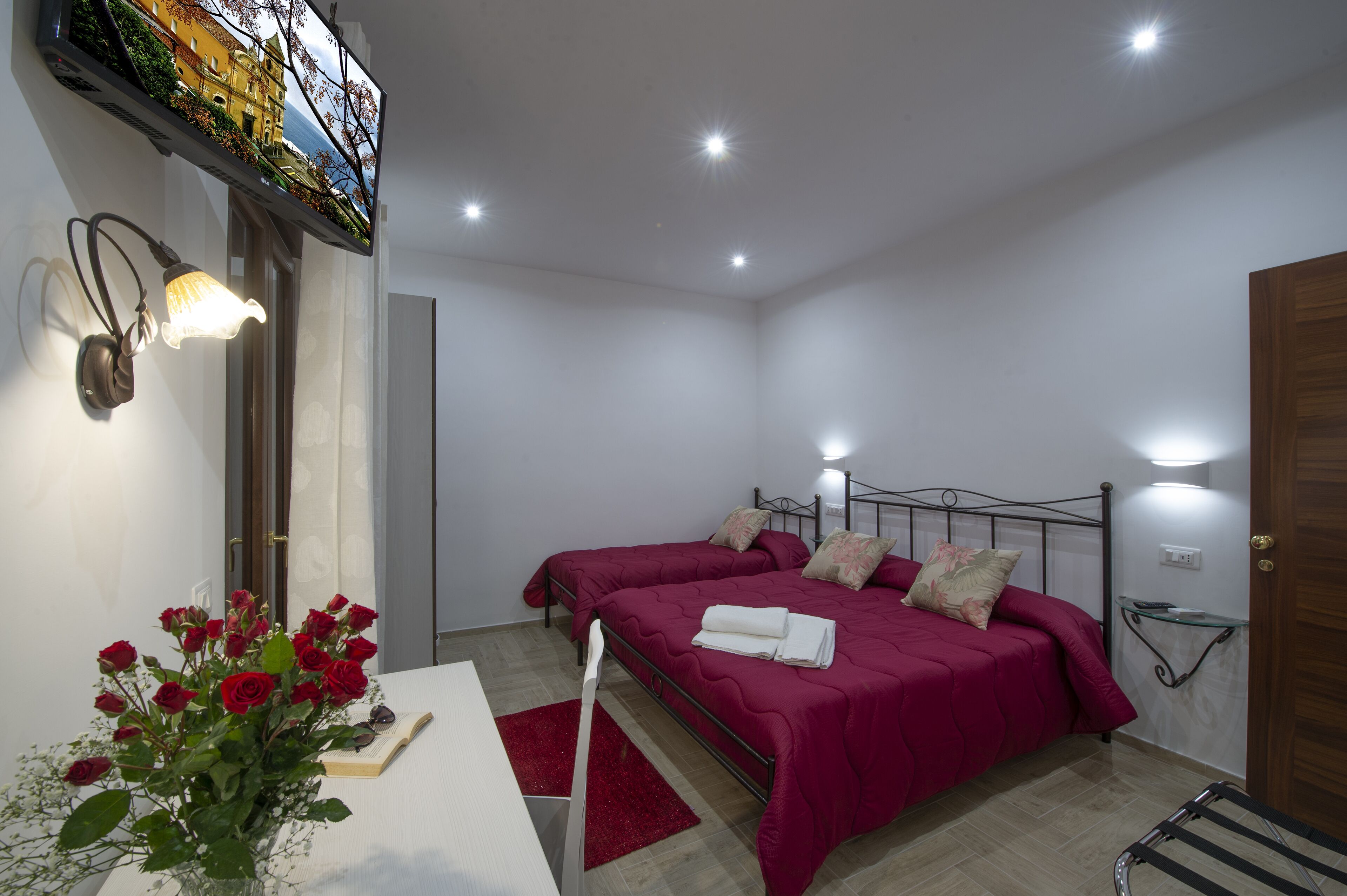 Une chambre avec deux lits, un bureau agrémenté d’un vase de fleurs et un téléviseur fixé au mur.