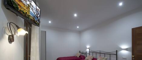 Une chambre avec deux lits, un bureau agrémenté d’un vase de fleurs et un téléviseur fixé au mur.