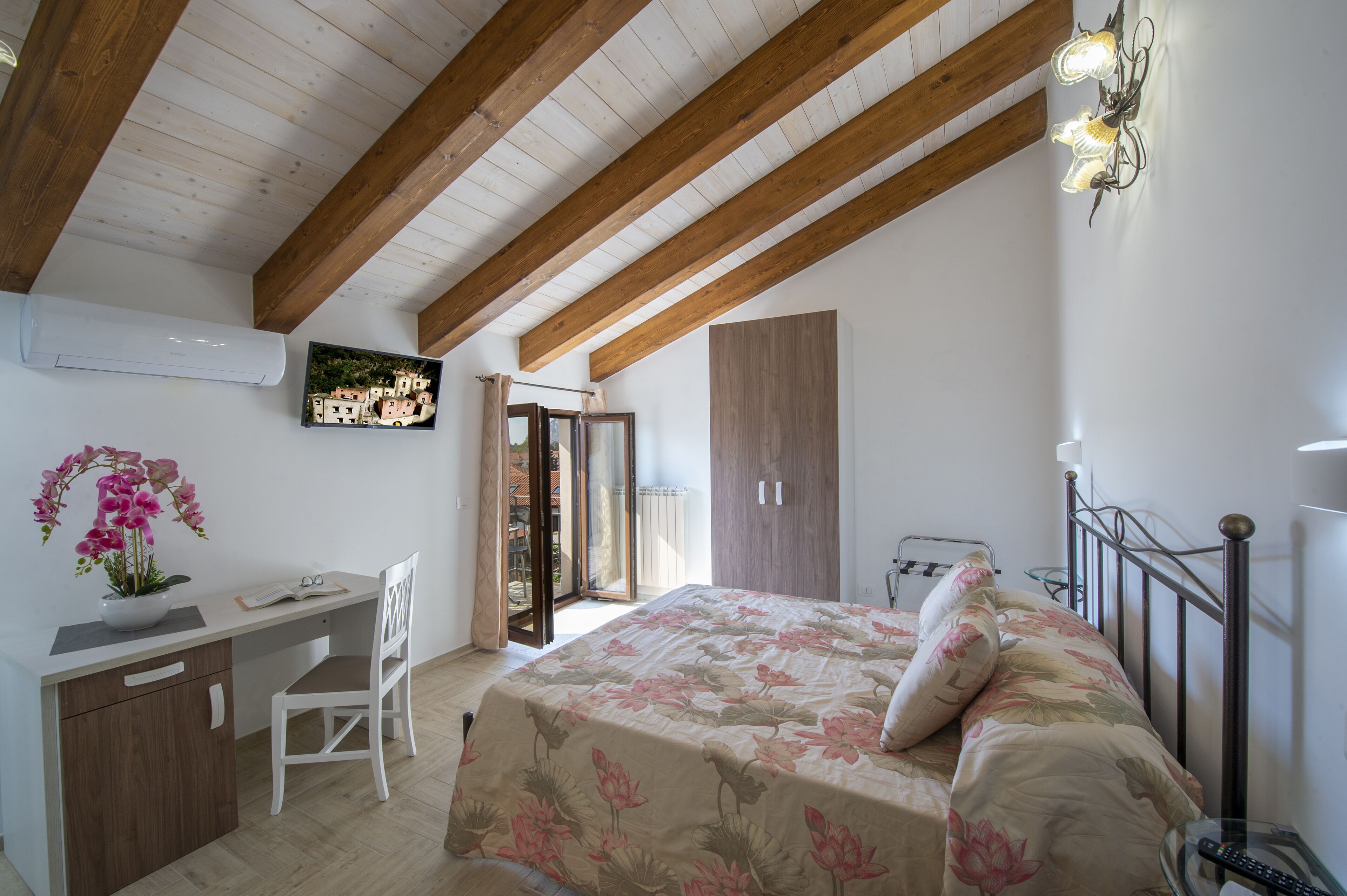 A bedroom with a bed, a desk, and a chair. There is a window with curtains, a door, and a painting on the wall.