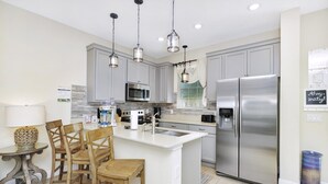 A modern kitchen with grey cabinets, stainless steel appliances, and a central island with bar stools.