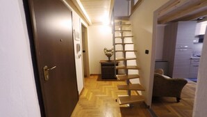 A narrow hallway with a wooden floor, a dark door on the left, and a staircase with a metal railing on the right. - Casa Bella del Borgo 2 (Bologna)