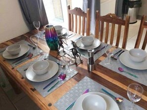 A wooden dining table set with plates, bowls, and cutlery, accompanied by a decorative vase and a salt shaker.