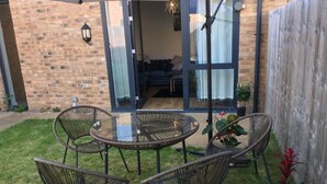 Une terrasse avec des chaises en osier et une table en verre, un mur en briques et une clôture en bois.
