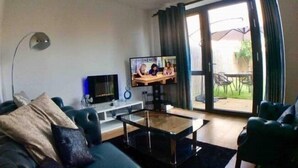 Un salon comprenant un canapé, une table basse, un téléviseur et une porte-fenêtre coulissante donnant sur un espace extérieur.