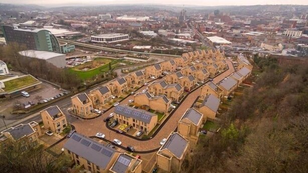 Un quartier résidentiel composé d’une rangée de maisons de ville, d’une cour centrale et d’un grand bâtiment en arrière-plan.