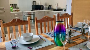 Une table à manger dressée avec des assiettes, des bols et des verres à vin, agrémentée d’un vase coloré et de sculptures en métal.