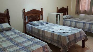 Una habitación con tres camas de madera, cada una con una colcha escocesa, y un refrigerador blanco en la esquina.