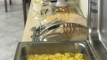 Montaje de bufé con diversas opciones de comida, entre ellas huevos revueltos, salchichas y un pastel.
