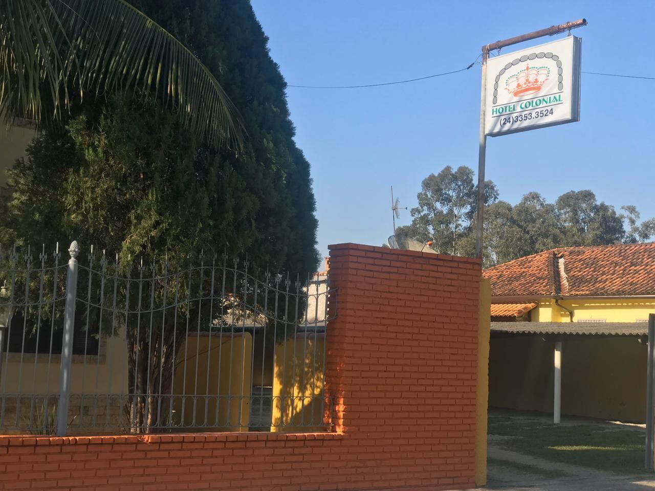 Un letrero de hotel con temática colonial, un área cercada y un edificio con techo de tejas.
