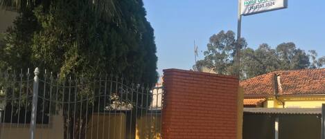 Un letrero de hotel con temática colonial, un área cercada y un edificio con techo de tejas.