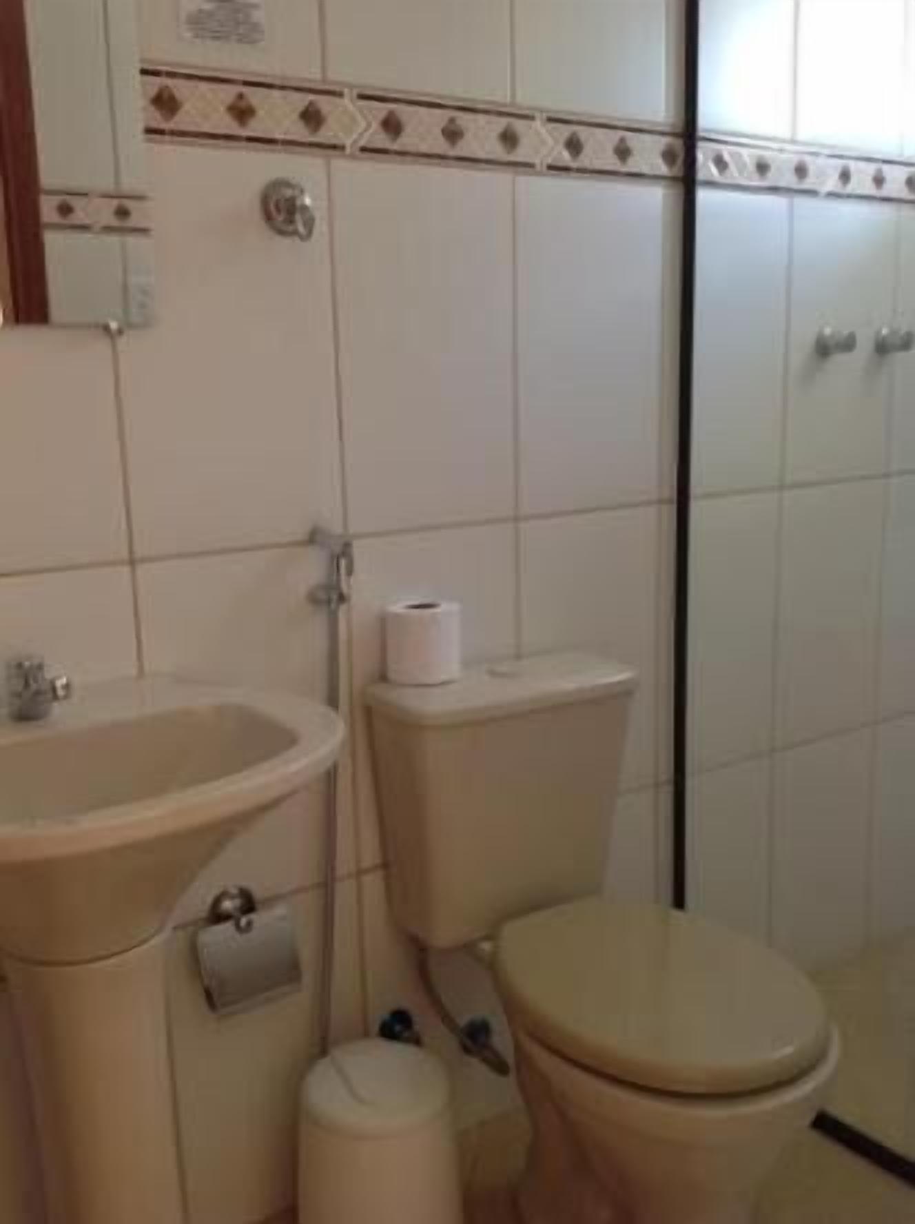 A bathroom with a sink, toilet, and a small trash bin.