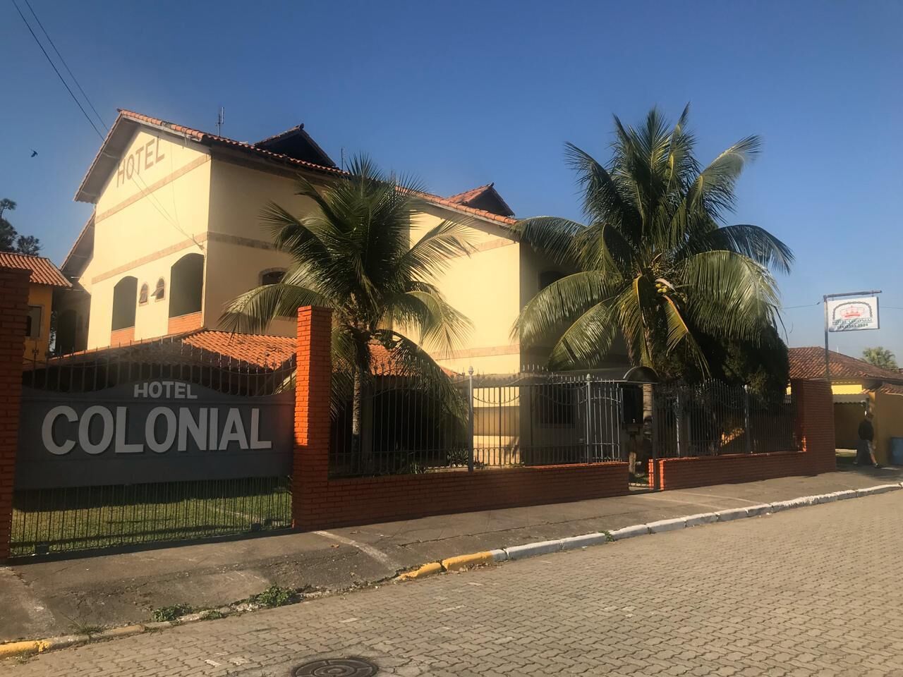 A colonial-style hotel with a prominent sign, palm trees, and a paved entrance.