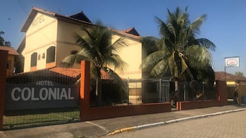 A colonial-style hotel with a prominent sign, palm trees, and a paved entrance.