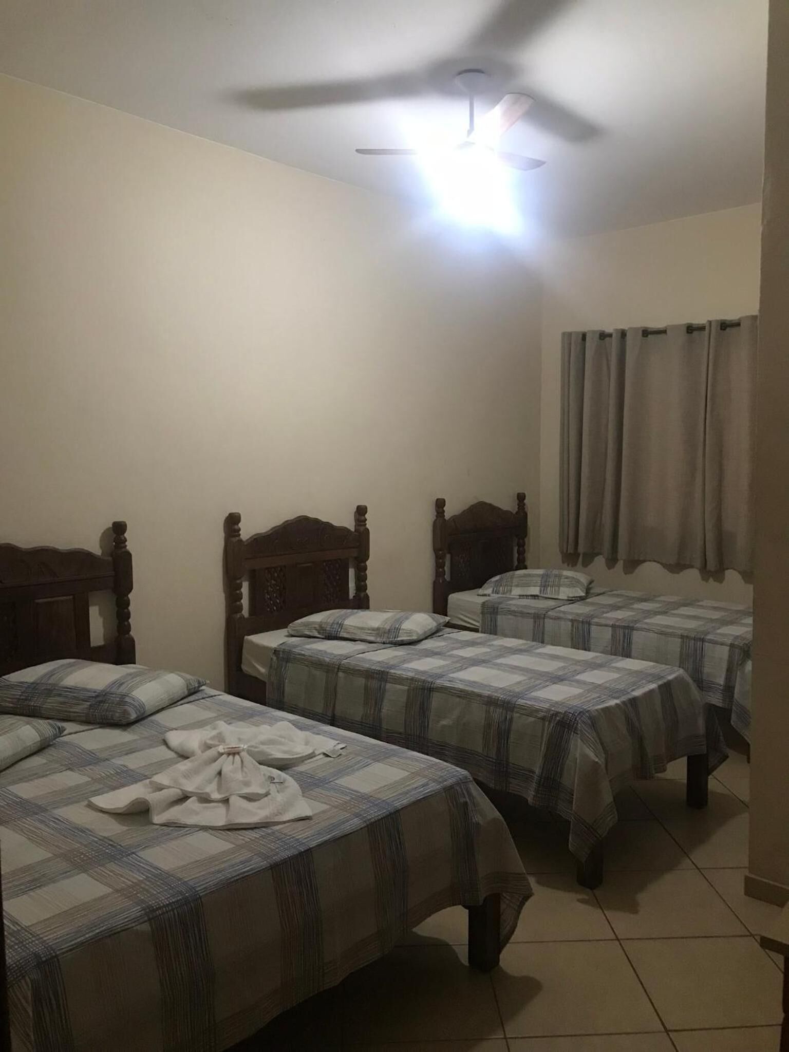 A room with three wooden beds, each with a plaid bedspread, a ceiling fan, and a light fixture.